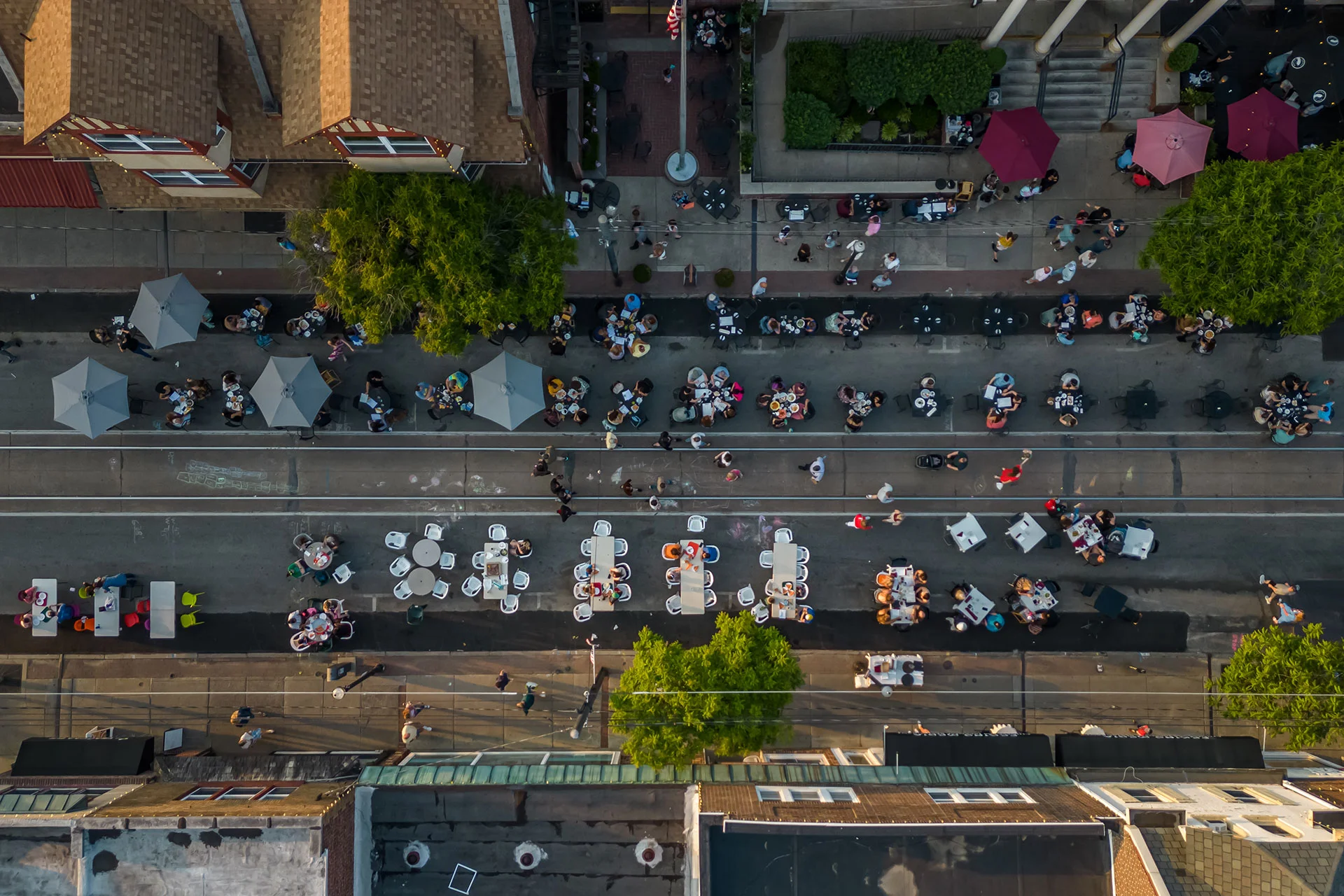 Aerial view of people dining outdoors on a closed street with tables and umbrellas during an evening community event